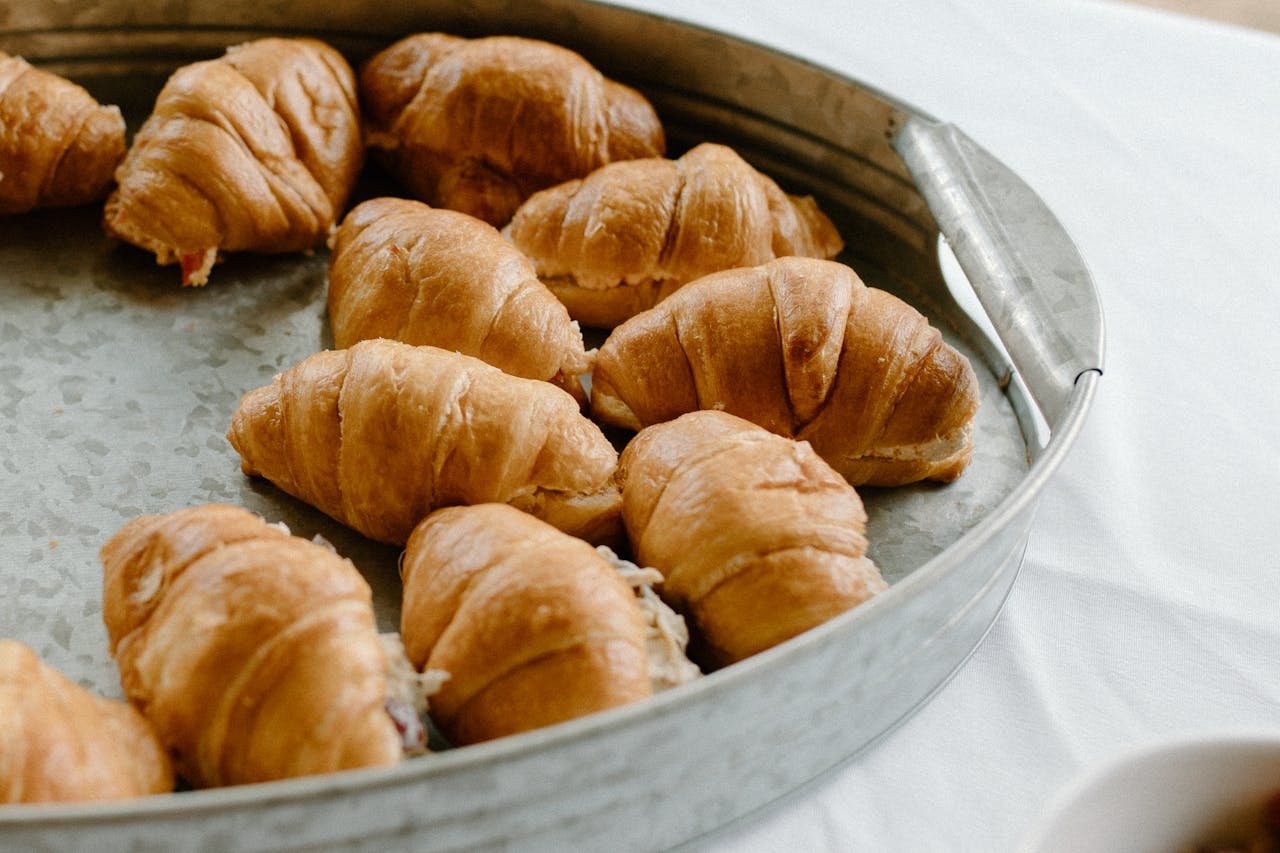 From above of baked croissants in tin tray prepared for dessert and placed on white table